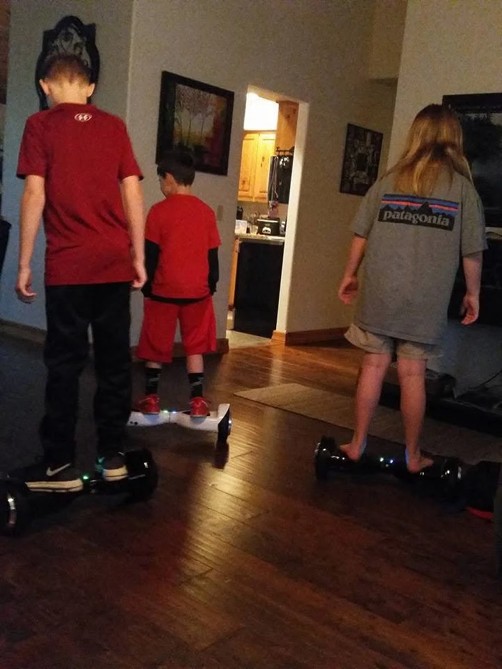 Three children riding hoverboards together in the living room.