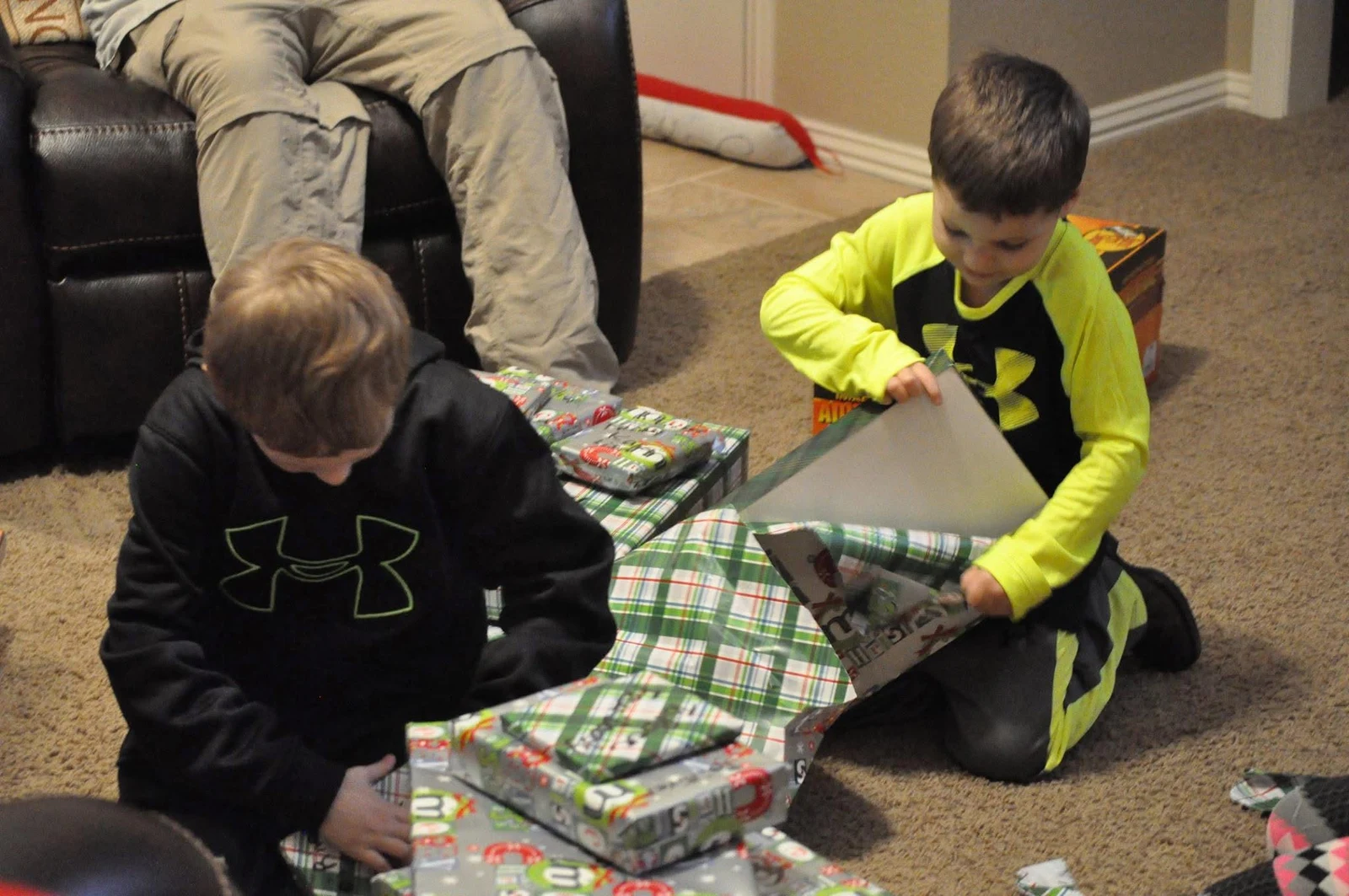 Two children in matching sports shirts unwrapping presents on the floor.