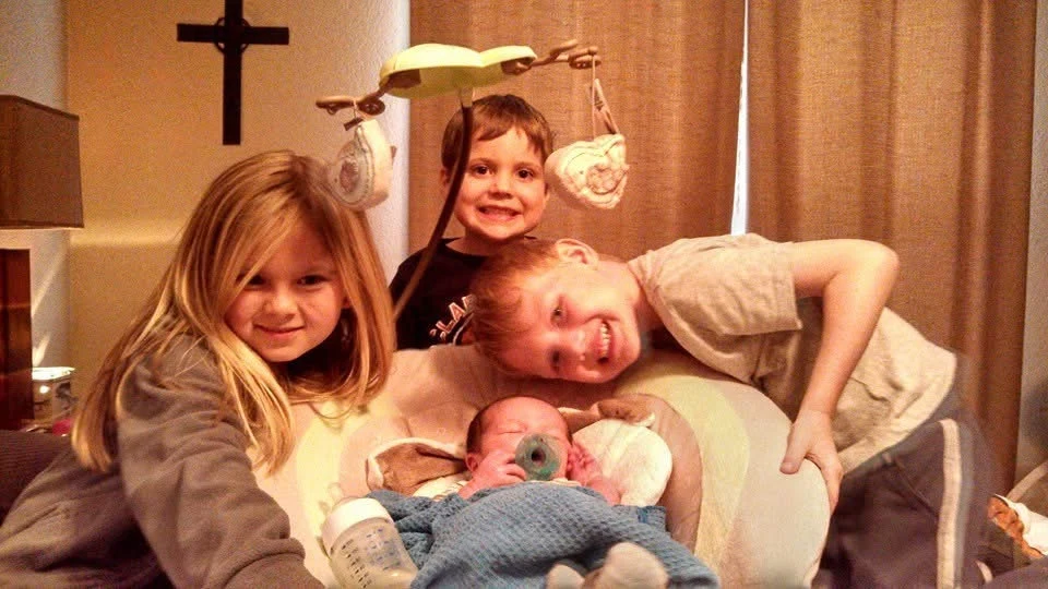 Three children gathered around a baby in a bouncer.