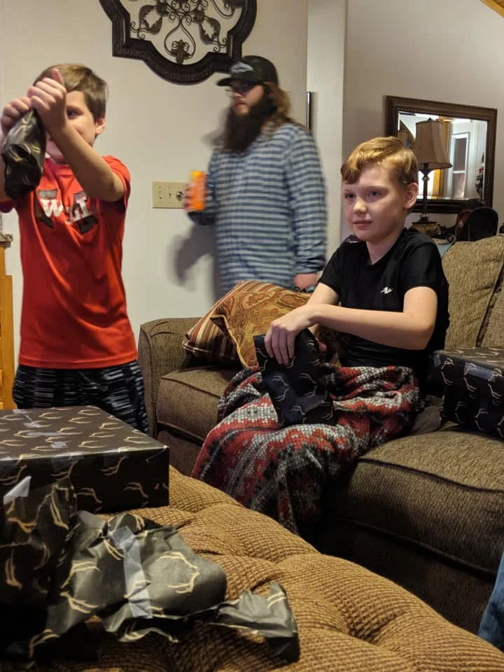 Two children opening presents by the couch, with an adult behind them.